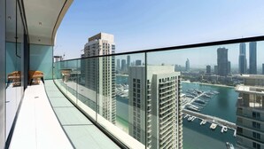 Un immeuble de grande hauteur doté d’un balcon en verre offrant une vue sur un port de plaisance et le paysage urbain.