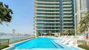 Un hôtel moderne doté d’une piscine à débordement sur le toit, de chaises longues blanches et offrant une vue sur le panorama urbain.