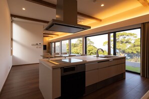 A modern kitchen with a large island, built-in appliances, and a view of trees through large windows.