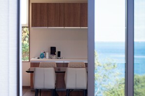A modern kitchen with wooden cabinets, a dining table with chairs, and a view of the sea through large windows.