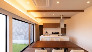 A modern kitchen with a wooden dining table and white chairs, a large window, and a brick wall. - Workation Resort THE Forest (Nagatoro)