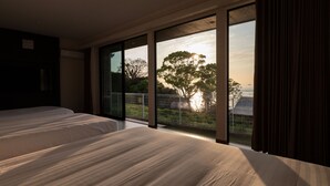 A bedroom with two beds, large windows, and a view of trees and a distant building. - Workation Resort THE Forest (Nagatoro)