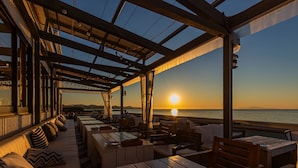 An outdoor seating area with tables and benches, overlooking the sea at sunset. - Workation Resort THE Forest (Nagatoro)