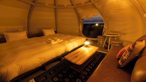 A tented accommodation with a bed, a small table, a chair, and a view of the night sky. - Workation Resort THE Forest (Nagatoro)