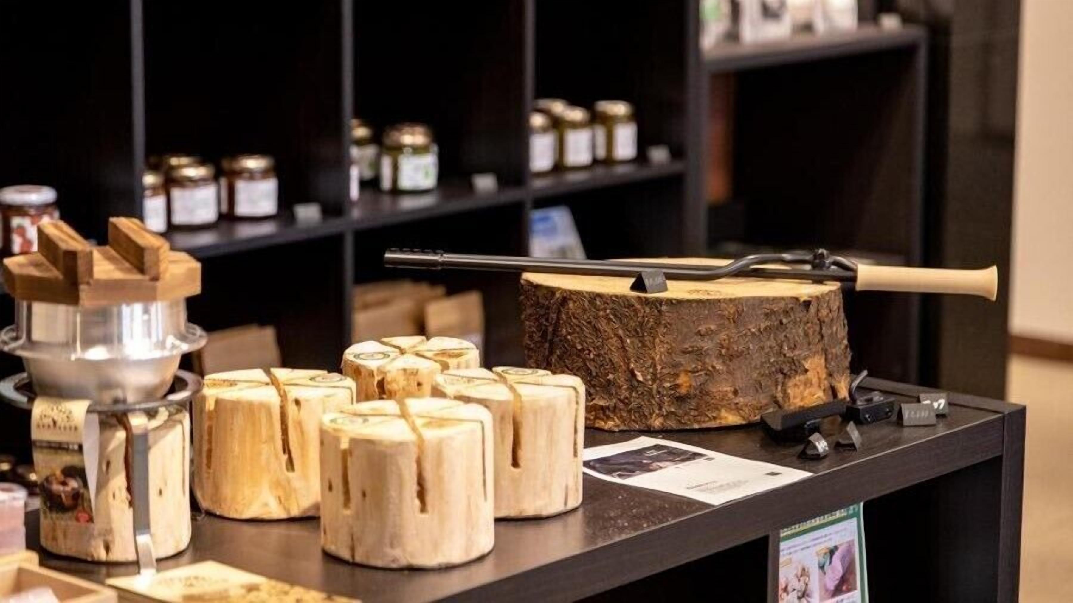 Holzklötze, ein Baumstumpf mit einem Gewehr auf einem Tisch, umgeben von Regalen mit Gläsern.