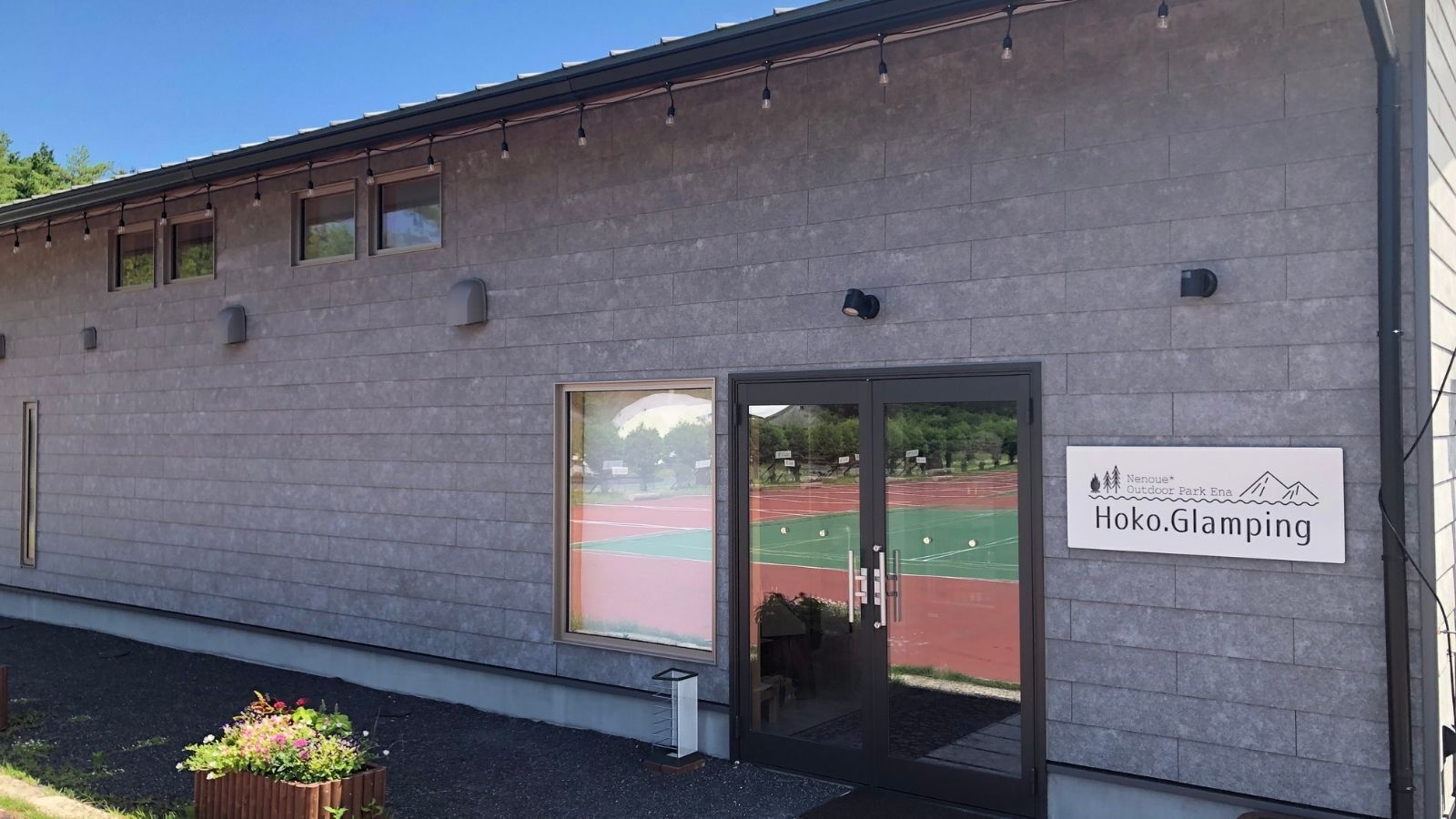 A building with a sign reading 'Hoko.Glamping' and a view of a sports field through a glass door.