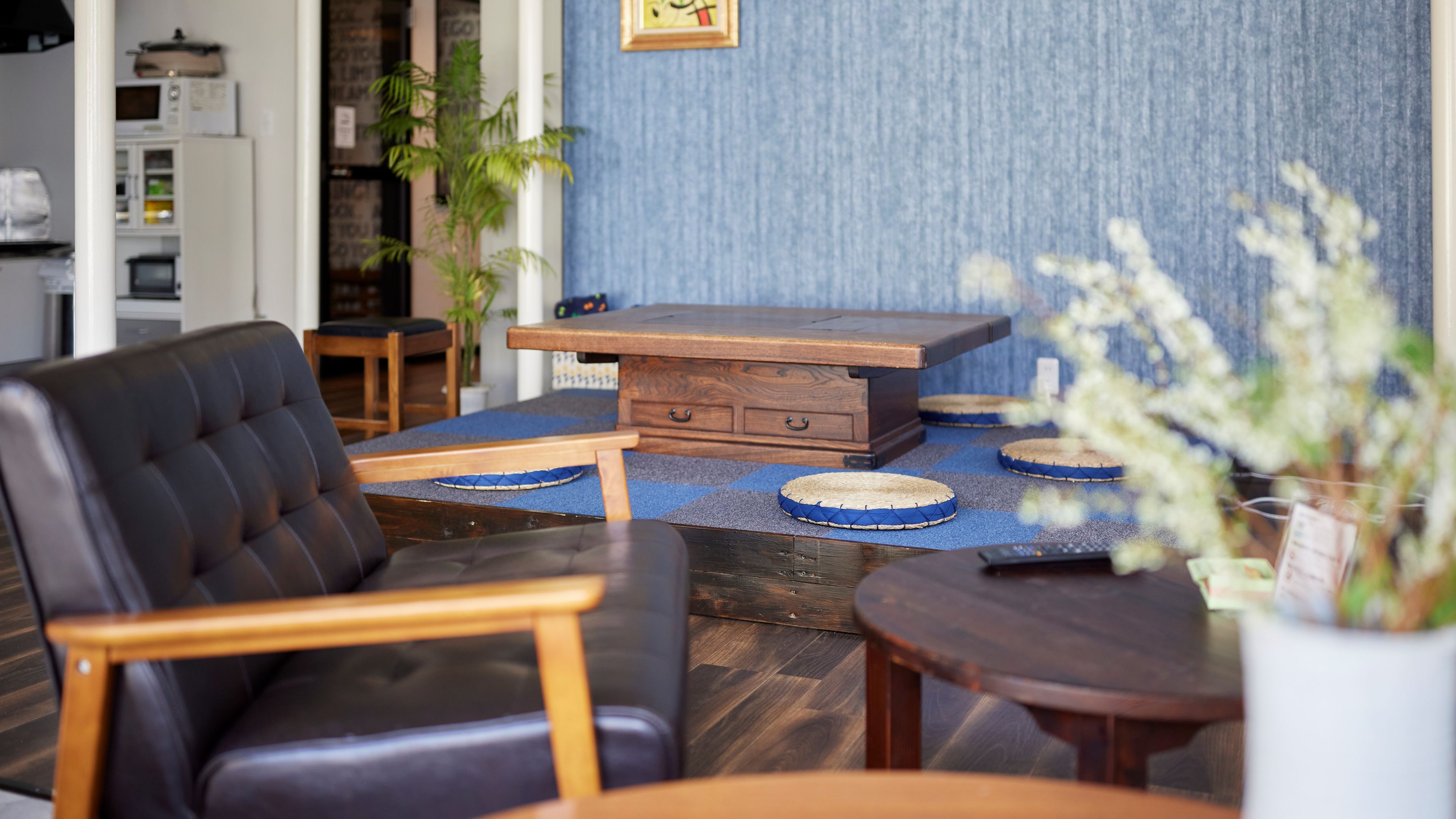 Una sala de estar moderna con un sofá de cuero, una mesa de centro de madera y una mesita auxiliar. Hay felpudos azules en el suelo y un mueble de madera al fondo.
