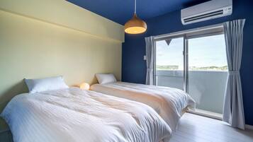 A bedroom with two beds, a hanging light fixture, an air conditioning unit, and a view of the outdoors through a sliding glass door.