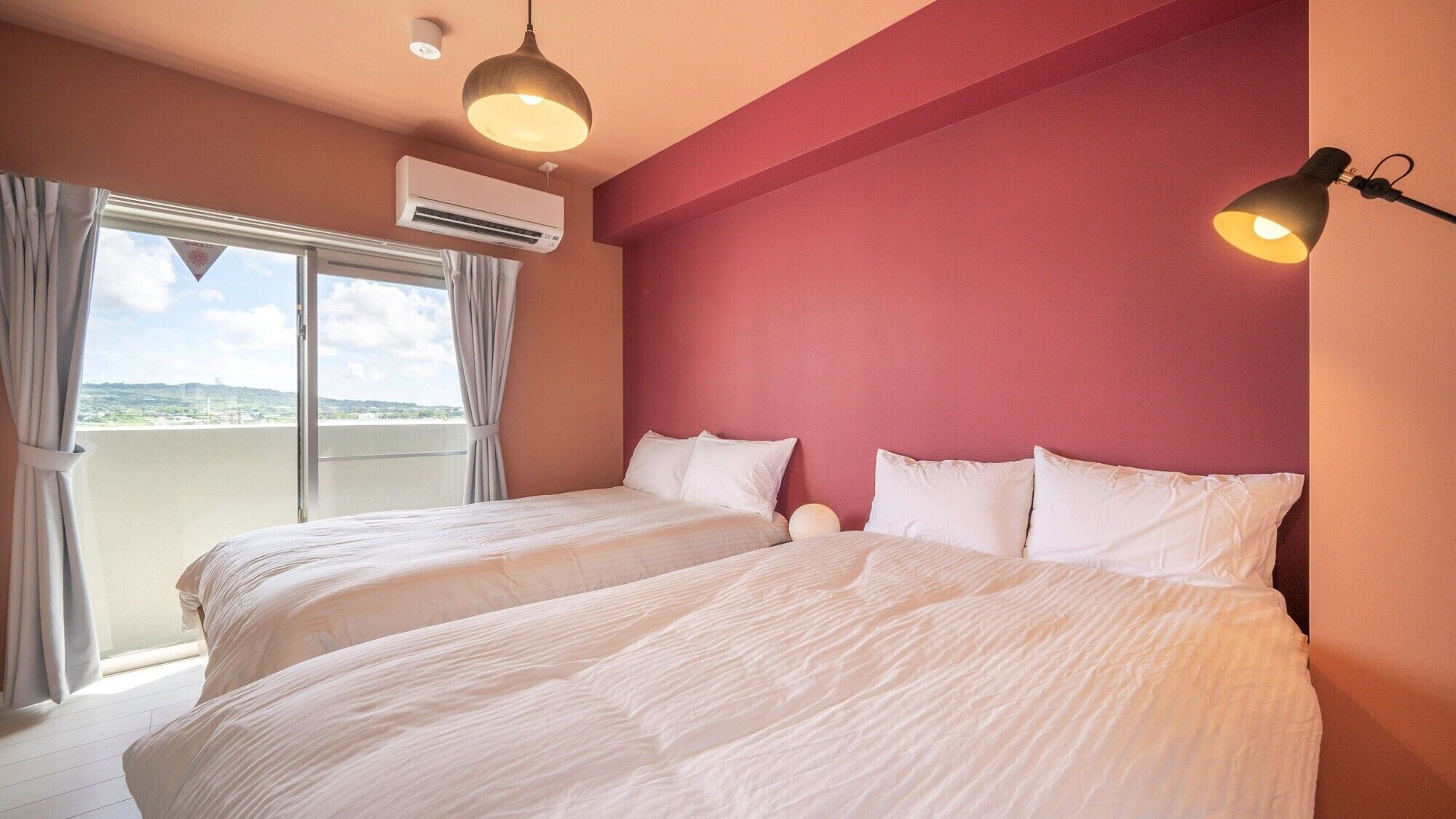Une chambre d’hôtel avec deux lits, une grande fenêtre avec des rideaux, un appareil de climatisation et un luminaire suspendu.