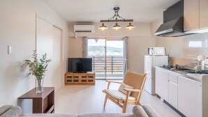 Un appartement moderne doté d’un balcon, d’une télévision, d’une cuisine et d’un fauteuil en osier.