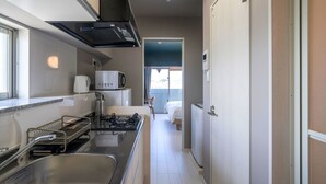 Une cuisine compacte équipée d’une cuisinière à gaz, d’un four à micro-ondes et d’un évier. On aperçoit un lit dans la pièce adjacente.