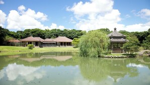 Un bâtiment de style japonais traditionnel, avec un étang devant, entouré de verdure et d’arbres.