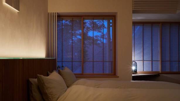 A bedroom with a large bed, a nightstand, and a window with a view of trees. - Toutou Onzaki Nikai no Yado (Kurashiki)