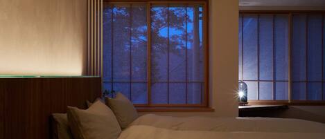 Une chambre à coucher avec un grand lit, une table de chevet et une fenêtre donnant sur des arbres.