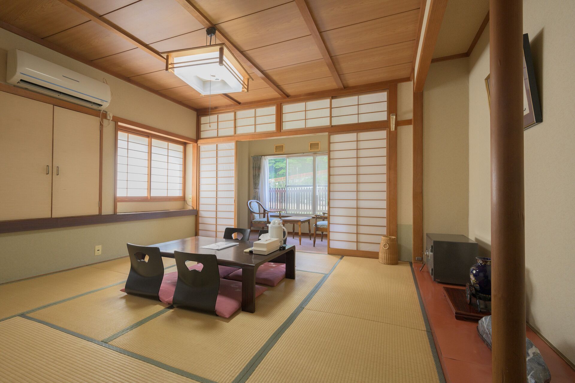 A traditional Japanese room with tatami flooring, a low table with cushions, sliding shoji doors, and a view of the outdoors.