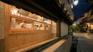 Pared exterior de madera con una ventana que muestra diferentes botellas y vasos, sugiriendo un ambiente de bar o restaurante.
