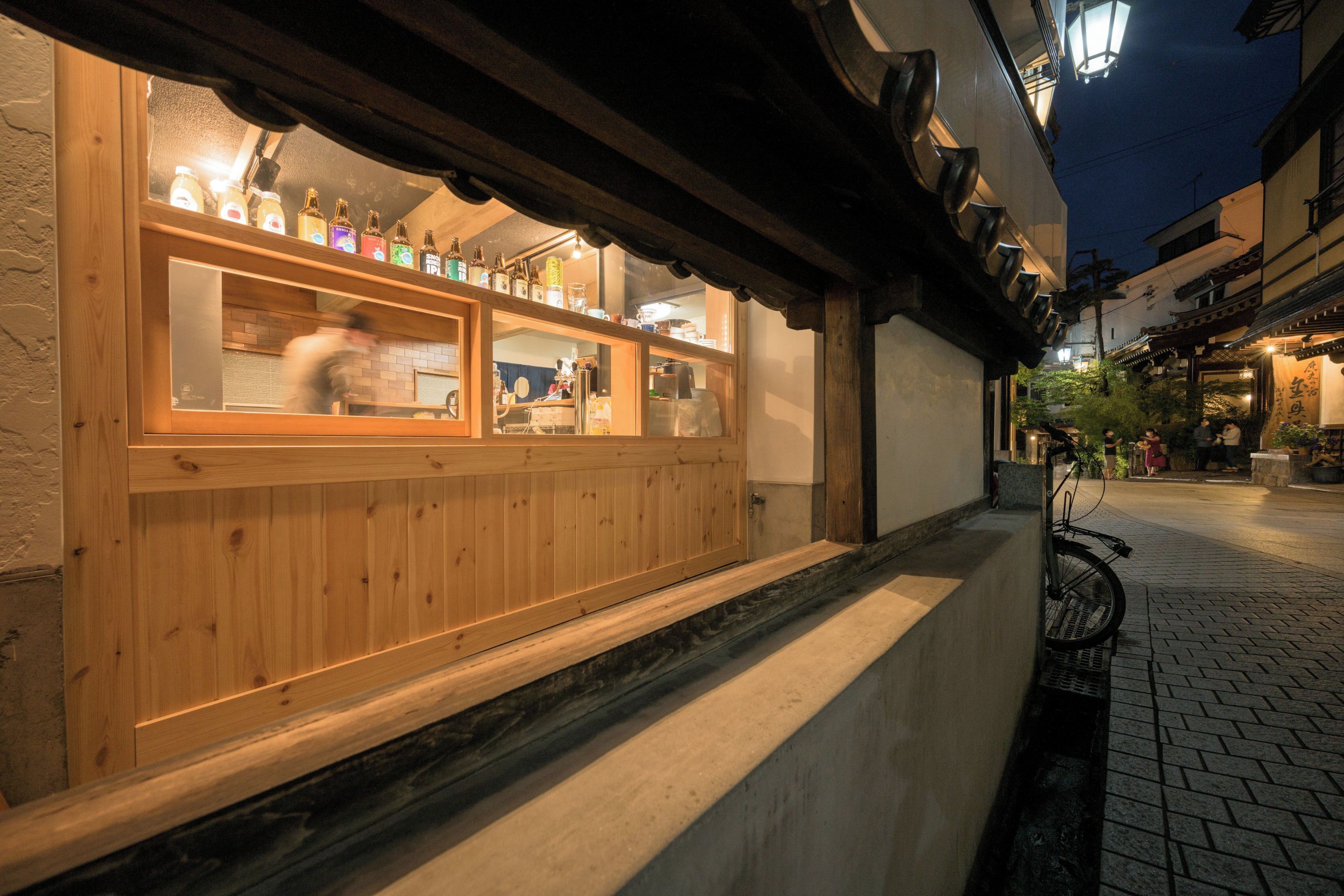 A traditional wooden building with a wooden counter and bottles visible through the window.