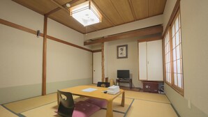 Una habitación tradicional japonesa con suelo de tatami, una mesa de madera baja, un televisor y puertas correderas.