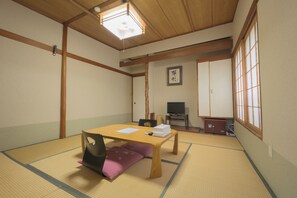 Een traditionele Japanse kamer met tatami vloeren, een lage houten tafel, een televisietoestel en schuifdeuren.
