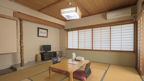 Una habitación japonesa tradicional con suelo de tatami, una mesa baja, un televisor y un amplio ventanal con pantalla shoji.