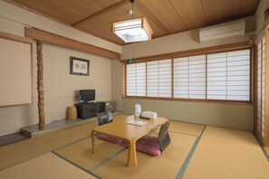 Een traditionele Japanse kamer met tatami vloerbedekking, een lage tafel, een televisie en een groot shoji-scherm raam.