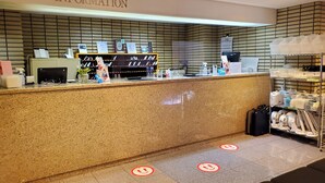 Et hotelreceptionsområde med en disk, informationsskilt og en vægmonteret hylde med forskellige genstande.