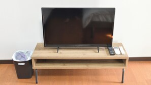 Un televisor sobre un soporte de madera, con mandos a distancia a su lado y un cubo de basura a la izquierda.