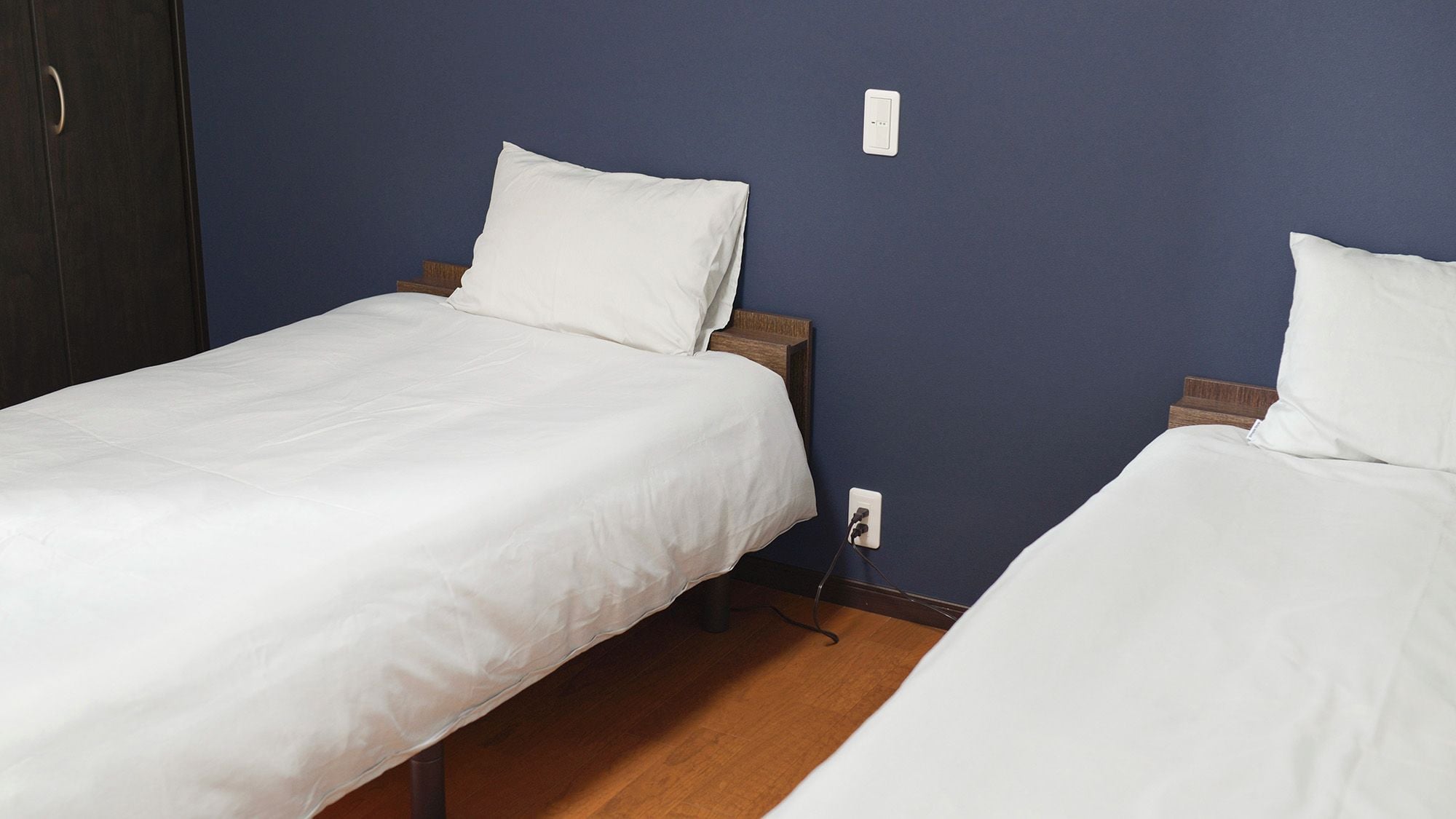 Una habitación con dos camas individuales, cabeceros de madera, ropa de cama blanca y un enchufe en la pared.
