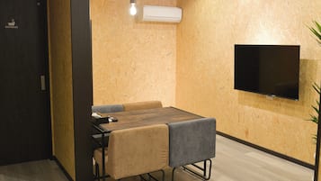 Una habitación compacta con una mesa de madera, dos sillas, un televisor montado en la pared y un equipo de aire acondicionado.