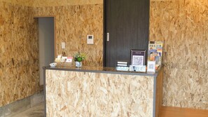 Mostrador de recepción con un fondo de madera, una planta en maceta, un reloj digital y folletos informativos.