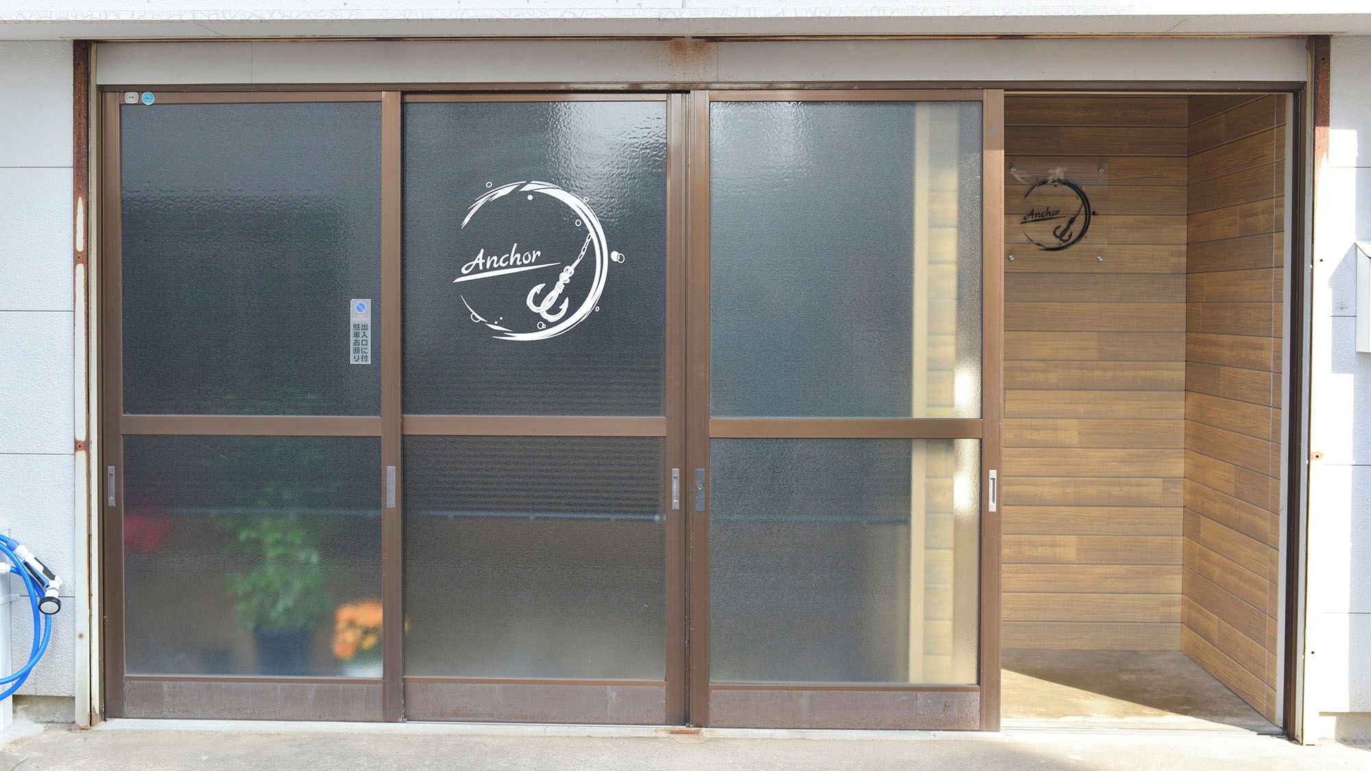Entrada de un edificio con puerta corredera de vidrio, logotipo en el interior y detalles de madera.