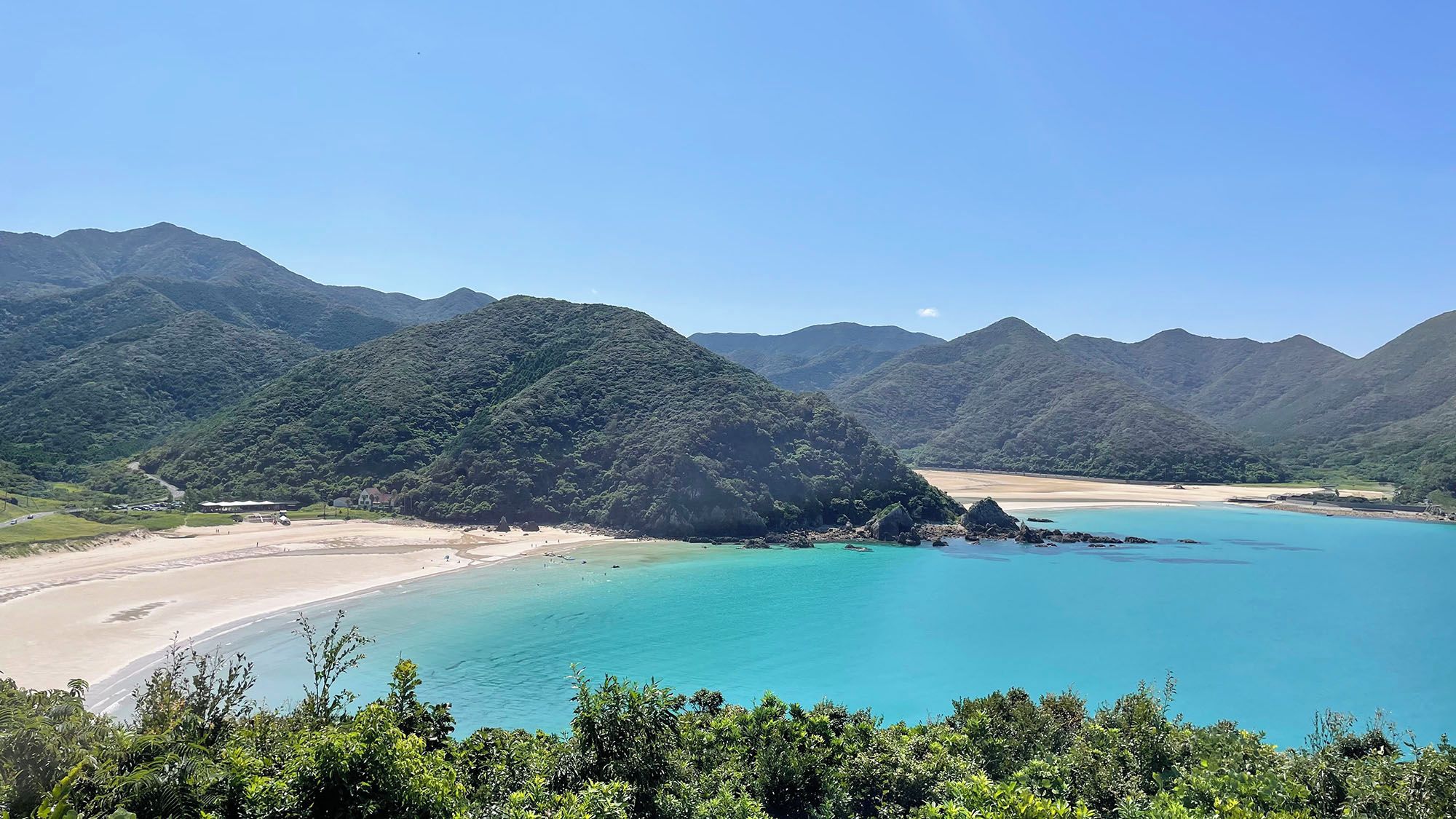 Un paisaje costero con una playa, aguas turquesas cristalinas y colinas verdes exuberantes.