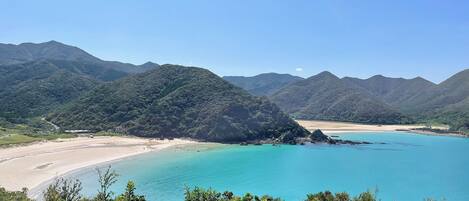 Un paisaje costero con una playa, aguas turquesas cristalinas y colinas verdes exuberantes.