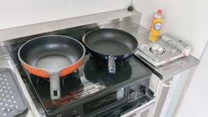 A kitchen with two frying pans on a stove, a bottle of cooking oil, and a portable electric stove. - Icony (Miyakojima)