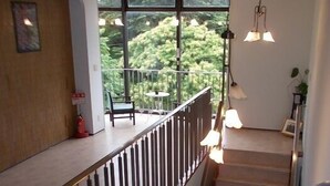 A staircase with a wooden handrail and metal balusters, leading to a balcony with a view of greenery. - Merci 0823 (Ito)