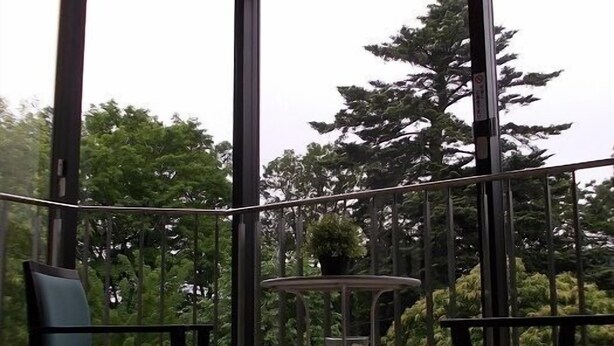 A balcony with a view of trees, two chairs, and a small table. - Merci 0823 (Ito)