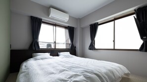 Habitación de hotel con una cama grande, dos ventanas con cortinas, un equipo de aire acondicionado y vistas al exterior.