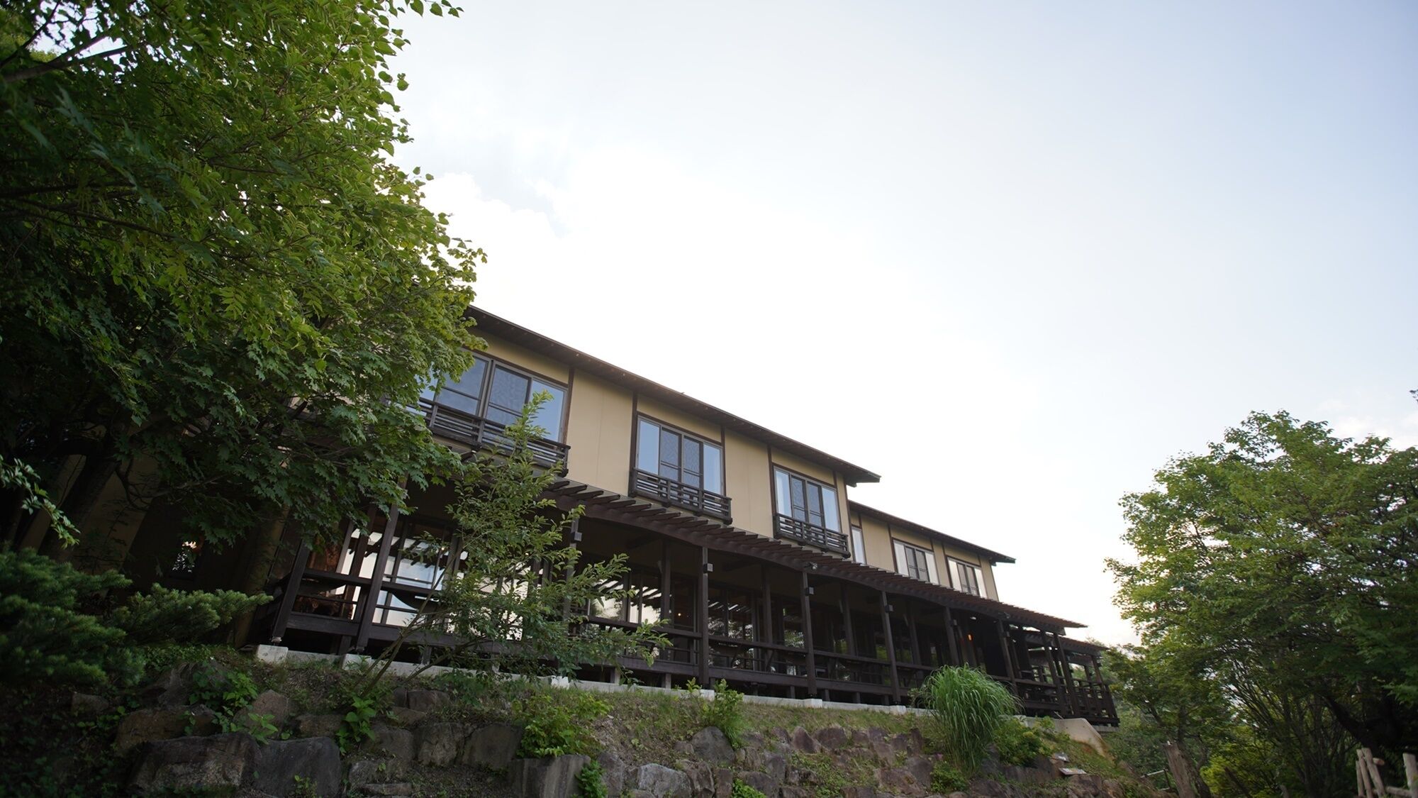 A two-story building with a balcony on the upper floor, surrounded by greenery.