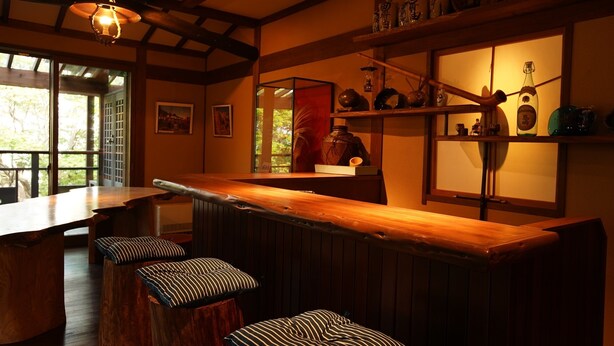 A cozy bar area with wooden stools, a high bar counter, and shelves with decorative items. - Kougetsu Okuyamada Onsen (Takayama)