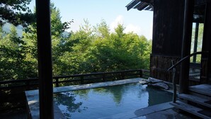 A wooden deck with a stone pool, surrounded by lush greenery and a wooden building. - Kougetsu Okuyamada Onsen (Takayama)