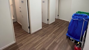 A hallway with three doors labeled "Shower Room 1", "Shower Room 2", and "Shower Room 3". There is a blue cart with a red fire extinguisher on the right side. - Lodges Daikoku (Toyama)
