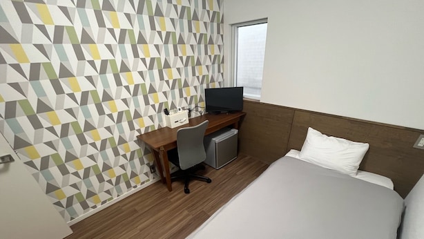 A hotel room with a bed, a desk with a computer, a TV, and a small refrigerator. - Lodges Daikoku (Toyama)
