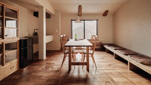 Een ruime eetruimte met een houten tafel en stoelen, een bank langs de muur, en een groot raam dat natuurlijk licht binnenlaat.