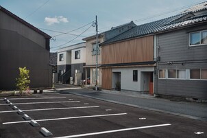 Un estacionamiento con espacios delimitados, edificios colindantes de arquitectura moderna y tradicional, y cielo despejado.