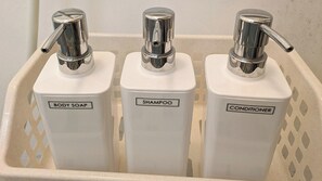 Three white dispensers labeled body soap, shampoo, and conditioner in a beige plastic basket.