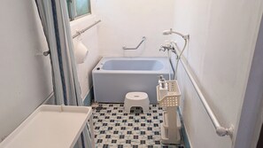 A small bathroom with a bathtub, a toilet, a handrail, and a window.