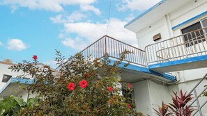 A residential building with a balcony, a water tank on the roof, and a garden with red flowers.