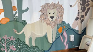 Habitación infantil con un mural de un león y una jirafa, una cama y una mesita de noche.