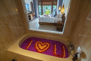 A bathroom with a bathtub, a shower, and a view of a bedroom with a bed and a balcony. - The Dura Ubud (Ubud)