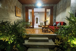 A hotel lobby with a staircase leading to a room, a red sofa, a wooden table, and potted plants. - The Dura Ubud (Ubud)
